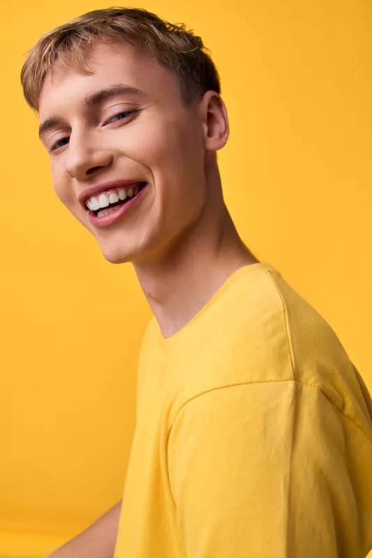 Smiling young man in a yellow shirt against a yellow background, conveying warmth, energy, and casual optimism suitable for lifestyle, fashion, and positive mood imagery