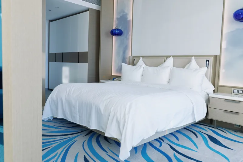 Hotel room with a large white bed, plush pillows and bold blue carpet offering a calm, modern retreat for rest and relaxation.