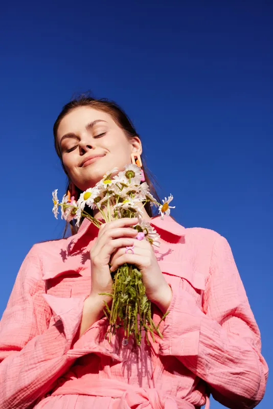 Young woman holding wildflowers against a clear blue sky, exuding happiness in a pink outfit Bright and cheerful summer atmosphere