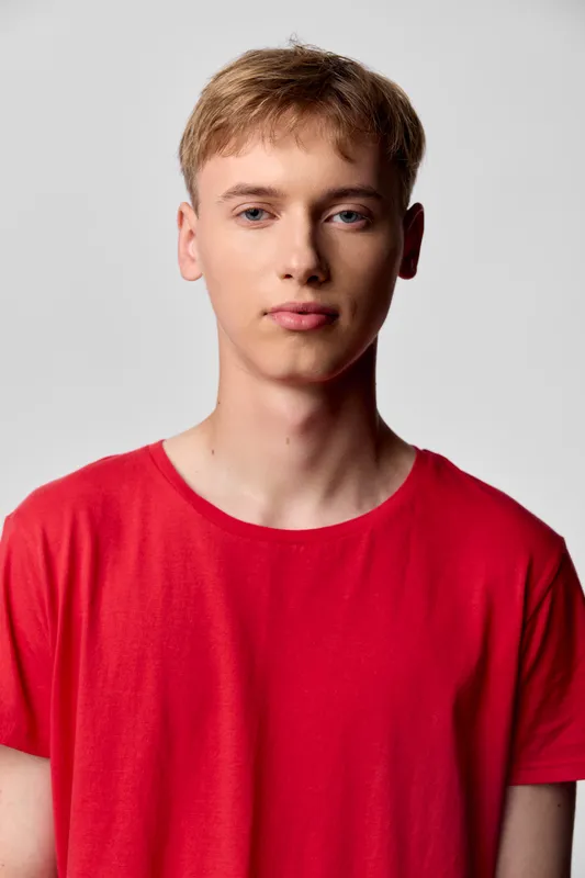Young male in a red casual t shirt stands against a neutral backdrop, clean lighting and minimal background suitable for fashion, lifestyle or stock imagery