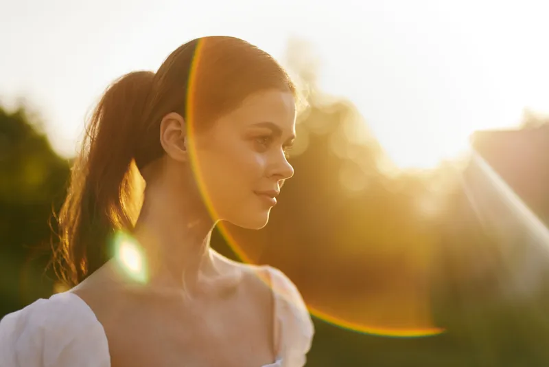 Beautiful young woman in a white dress enjoying sunlight, vibrant colors, emotional connection, nature background, serene atmosphere, outdoor portrait