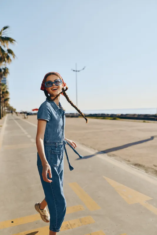 Lifestyle woman in modern boho-western denim street style with sunglasses and a braided hairstyle enjoying sunny weather, film color effect enhances warm vibrant tones.