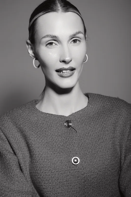 Elegant Caucasian woman with pale skin wearing earrings and textured sweater in black and white portrait studio. Sophisticated mood.