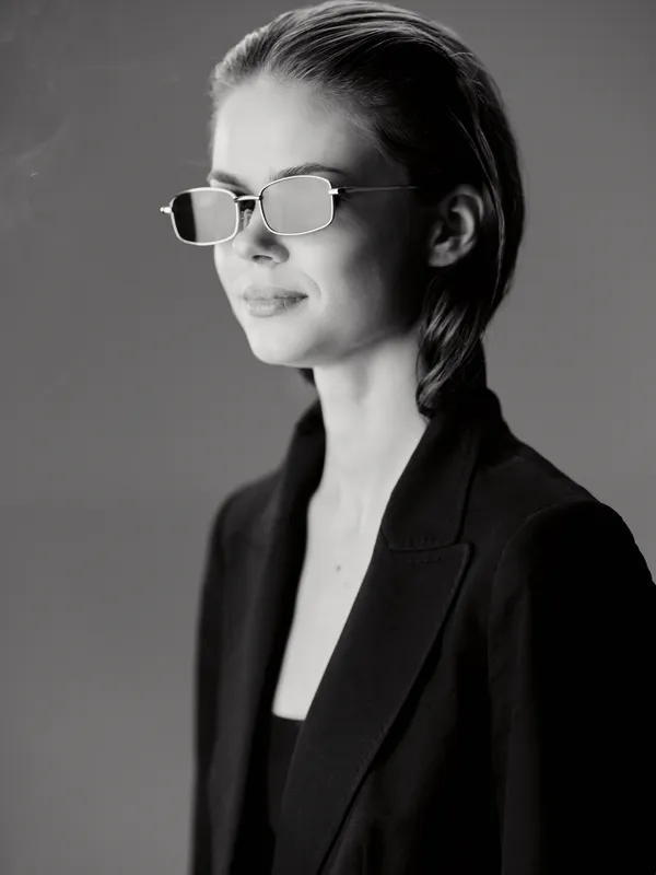 Black and white portrait of a stylish woman wearing sunglasses and a blazer, showing confidence and chic fashion style.