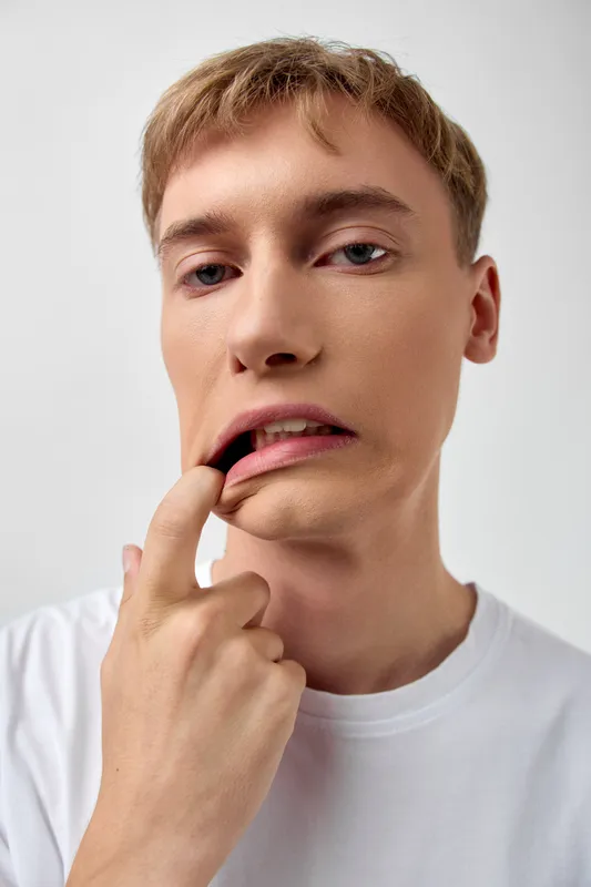 Closeup of a man biting his finger, an expression of anxiety and temptation, lips and gaze revealing emotion, casual white shirt and soft lighting creating a moody everyday moment