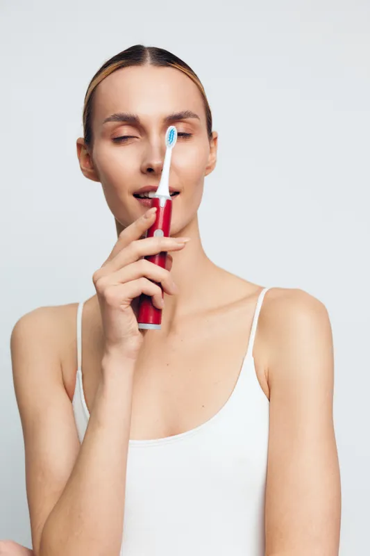 A woman brushes her teeth with a red toothbrush, eyes closed in a calm moment, showcasing daily dental care and fresh breath, wellness and self care.