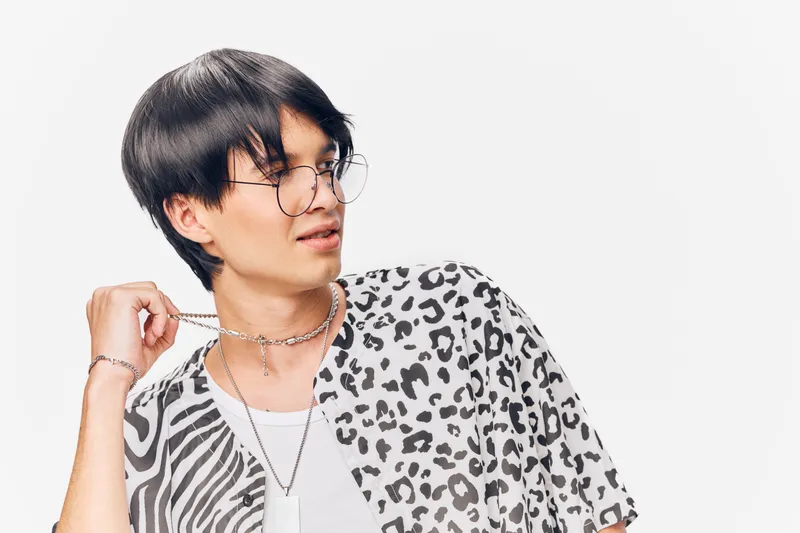Young man wearing glasses and animal print shirt poses with playful expression on white background in casual style with trendy accessories.