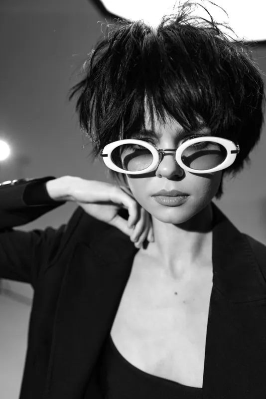 Stylish woman wearing white sunglasses and black jacket in black and white artistic portrait.
