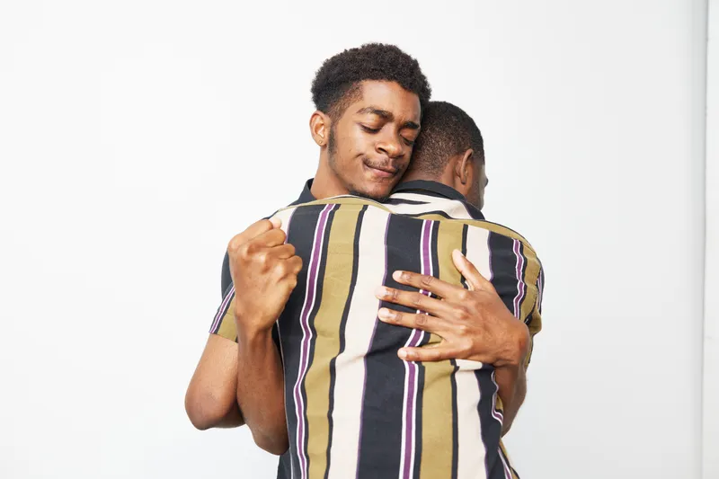 Two black men embracing each other in a warm moment, showcasing love and friendship against a clean background, highlighting strong emotional connection.