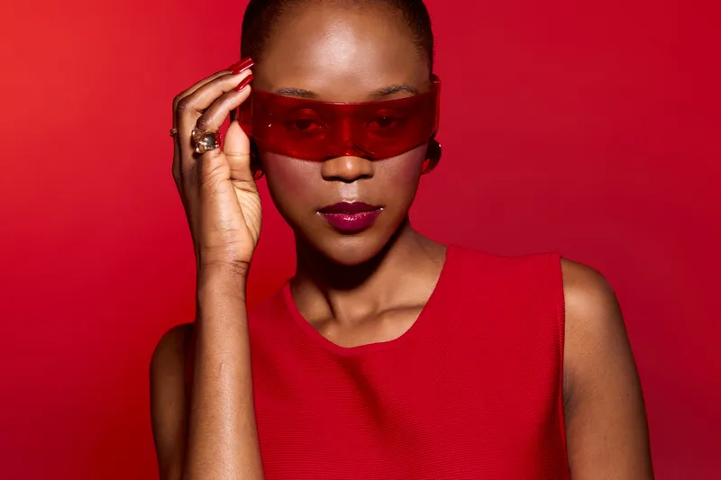 Confident dark skinned African woman in red dress and red sunglasses poses against a red background. Concept of fashion, style, beauty, and elegance with bold colors and modern look.