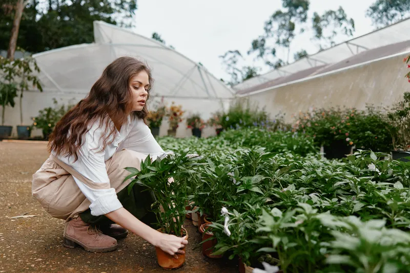 Young woman tending to potted plants in a greenhouse, showcasing sustainable gardening, nurturing emotions, and a fresh green environment