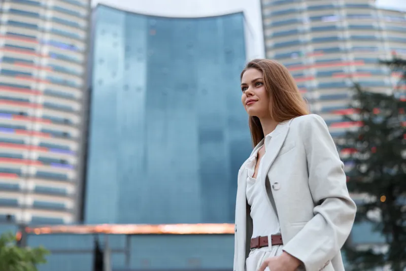 confident woman in beige business suit standing with modern office building background, urban business concept, professional attire and ambition