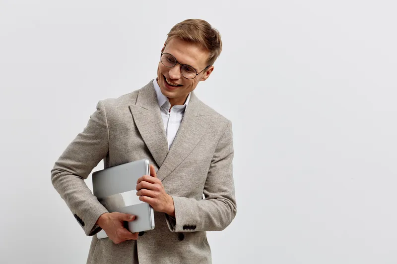 smiling young caucasian man hold laptop wear beige coat glasses standing isolated on light background digital nomad work concept