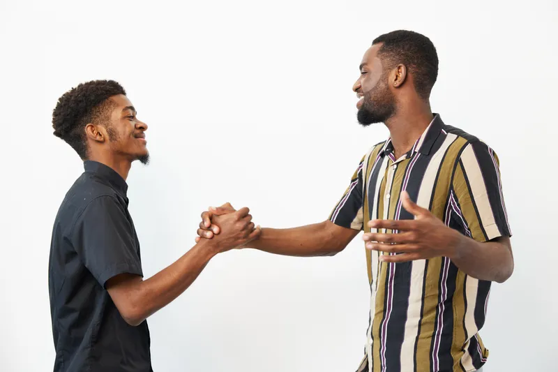 Two African American men smiling and greeting each other warmly, showcasing friendship and connection in a bright, modern setting. Concept: joy of connection.