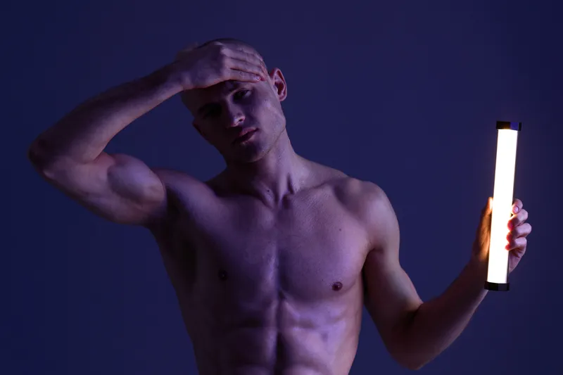 Striking image of a shirtless man holding a light tube, showcasing emotion and intensity in the dark setting. The low light creates a dramatic atmosphere.