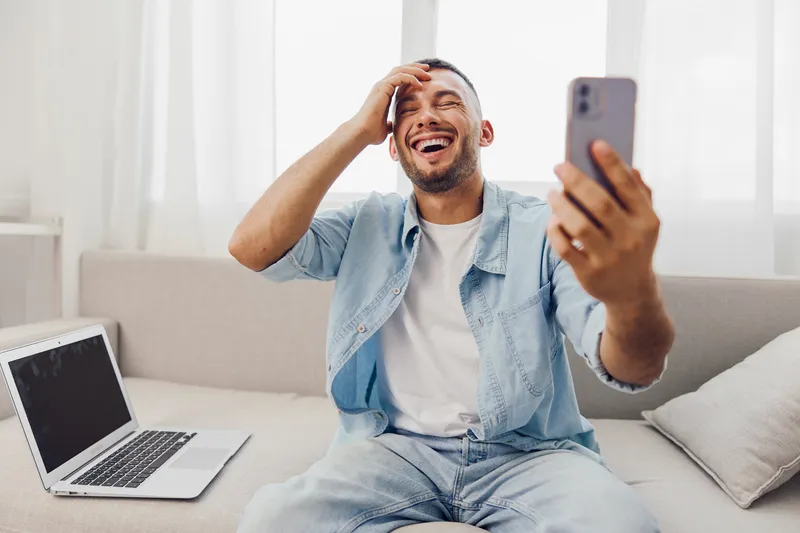 Laughing man engaging in a phone call, embodying vulnerability, emotional connection, and mental well-being at home amidst a digital detox.