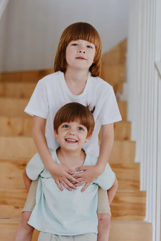 Two cheerful boys playfully pose on a staircase, radiating joy and energy. Their playful interaction captures the essence of childhood friendship and fun.
