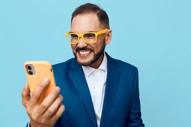 A confident business professional man on a vibrant colored background, isolated. He smiles while looking at his phone, projecting energy, focus, and ambition.