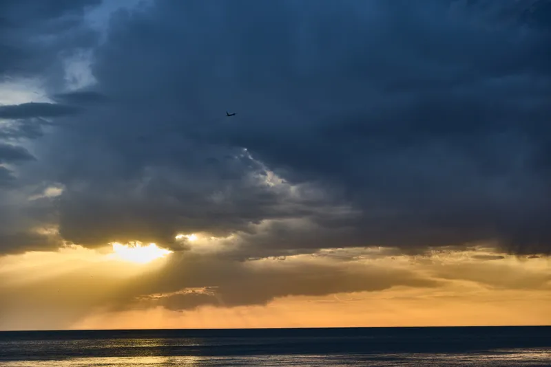 dramatic sky over calm sea with sunset and airplane in twilight evening scene KEYWORDS: sunset sky sea airplane twilight clouds horizon evening ocean sunlight rays storm weather nature scenic mood sun