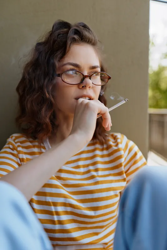 Candid woman outdoors, thoughtful pose, casual striped shirt, glasses, sunlight, relaxed mood, contemplative moment, warm tones, natural backdrop, subtle breeze, quiet confidence