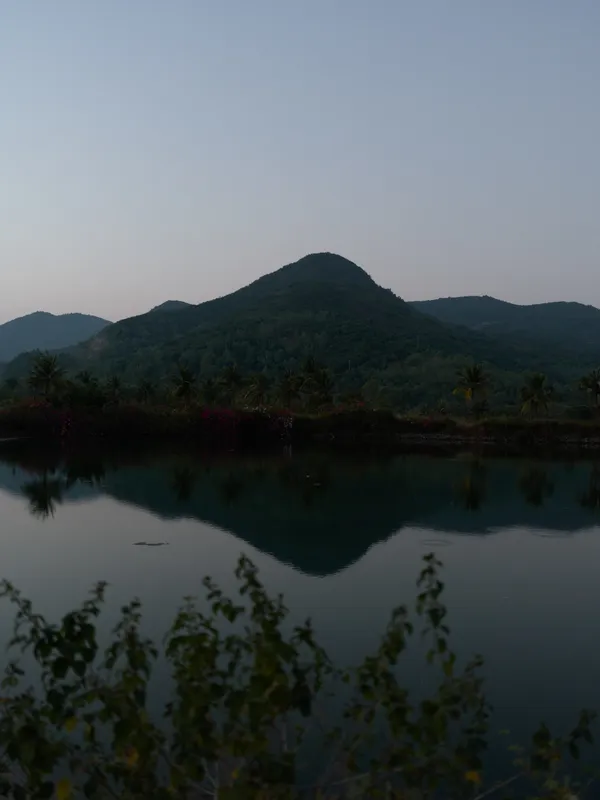 peaceful mountain landscape reflected in calm lake water during early morning, surrounded by lush green trees and soft natural light, serene nature scene