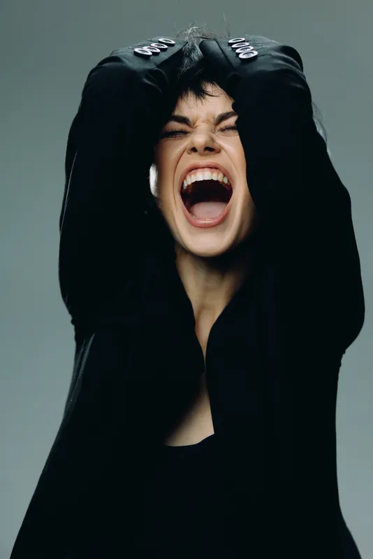 screaming woman in black clothing expressing strong emotion with closed eyes and raised hands
