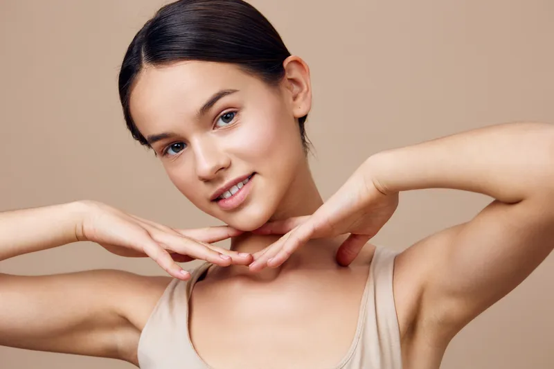Young female model with light skin and a serene expression, wearing a beige top, showcasing natural beauty against a soft, neutral background