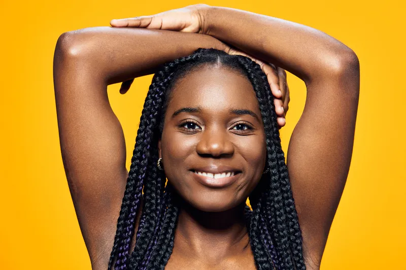 Happy young African woman with braided hair posing against a bright yellow background, conveying joy and confidence