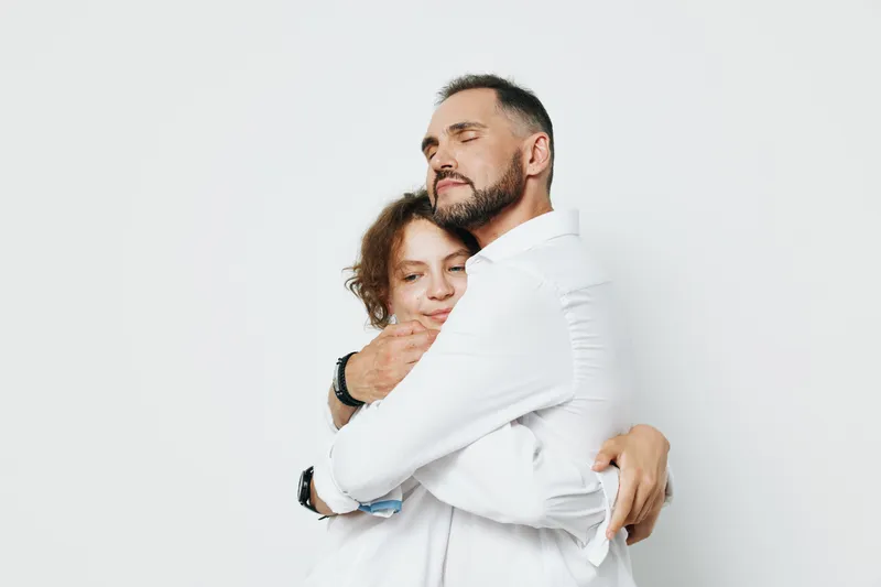 A professional man embraces a colleague in a warm moment on a clean bright backdrop, conveying emotion, support, and teamwork suitable for business, leadership, and success messaging.