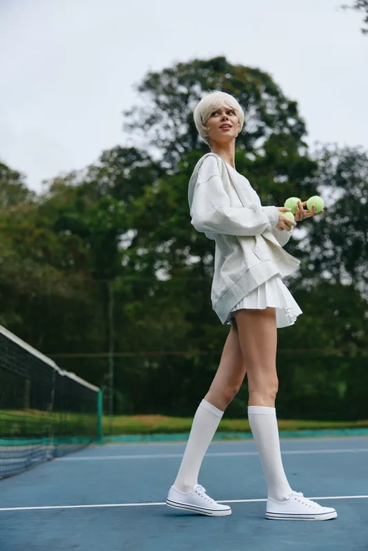 Young woman in sporty outfit holding tennis balls on the court, showcasing an energetic and positive vibe, perfect for promotional seasonal sports content