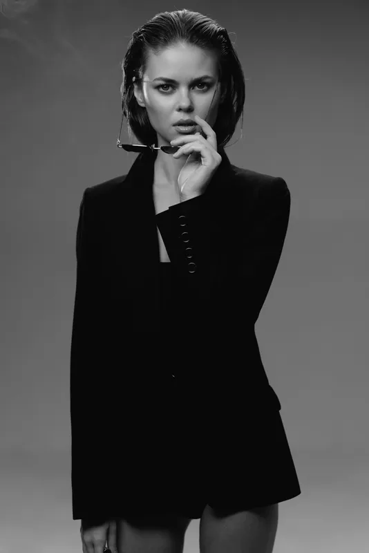 Black and white portrait of a serious woman wearing a blazer with wet hair and glasses in hand
