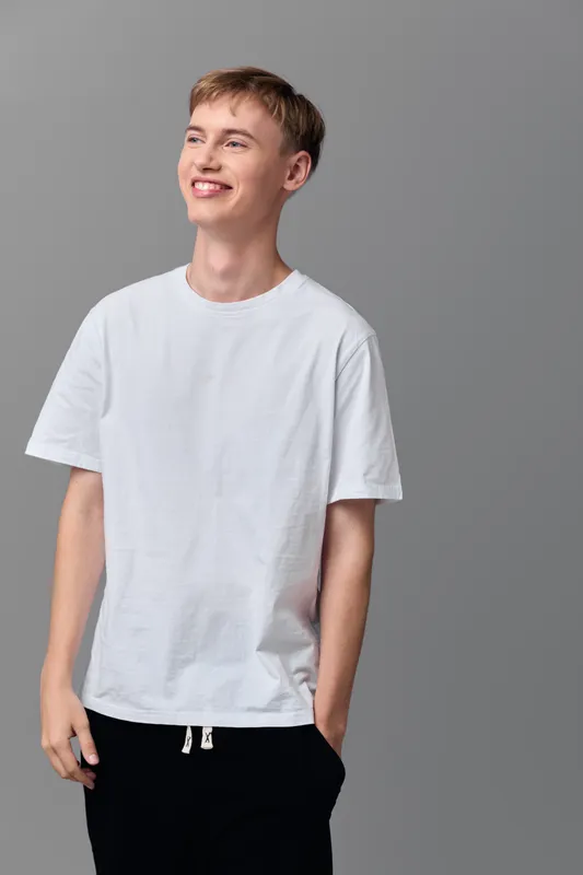 Casual man in a white t shirt standing in a studio, relaxed smile, simple fashion shoot, everyday wear, confident casual style for lifestyle and apparel branding