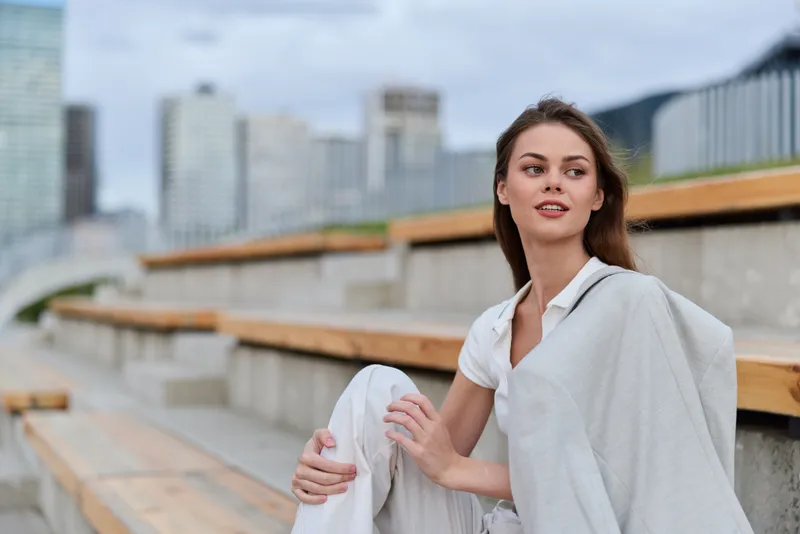 Business woman sitting outdoors, exuding confidence in a modern urban setting with a soft palette and stylish attire.