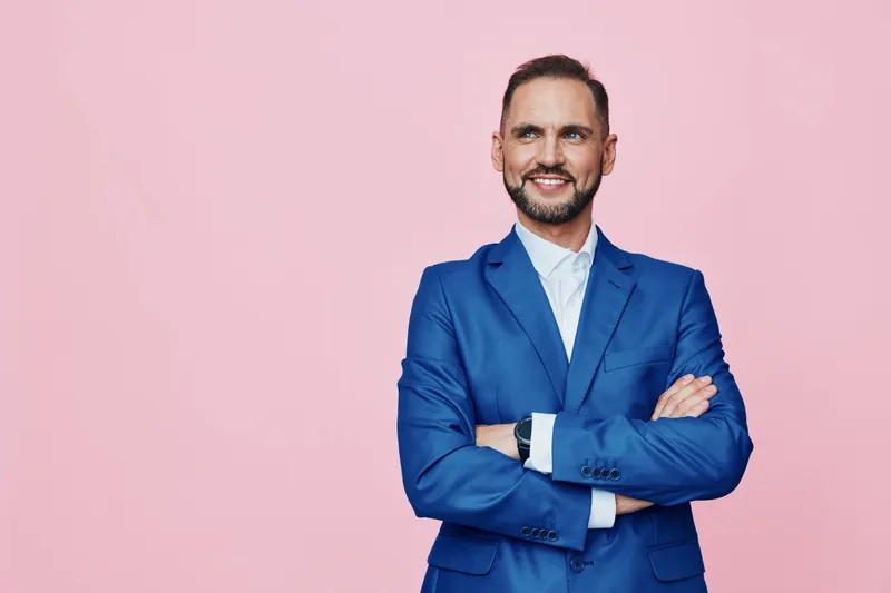Professional man in a blue suit stands confidently against a soft pink background, radiating focus and assurance. An isolated colored backdrop highlights his poised expression and strong business