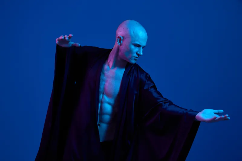 Dynamic man striking a pose in a dramatic blue light setting, showcasing strength and artistry. Stylish attire enhances vibrant mood and modern aesthetics.