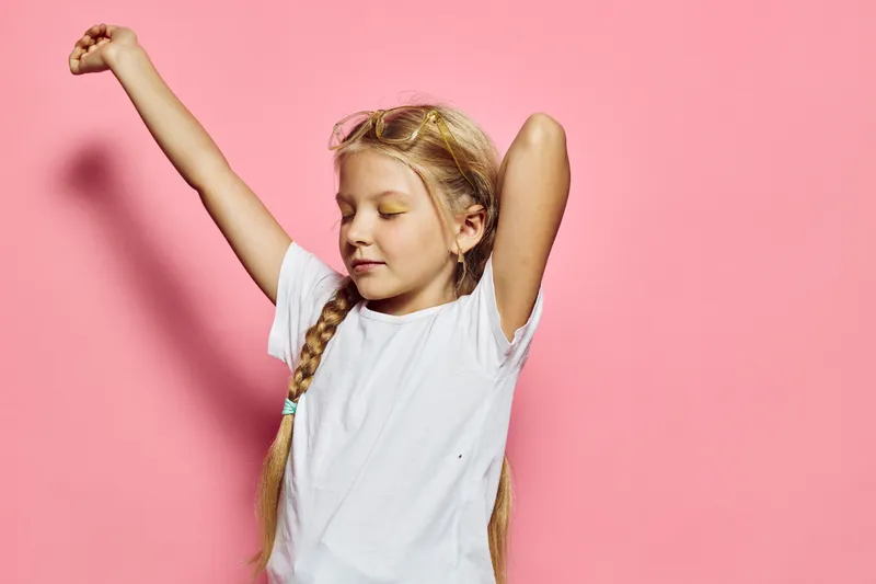 Young girl with braided hair stretching arms and closing eyes in white t-shirt on pink background. Concept of childhood, relaxation, and comfort.