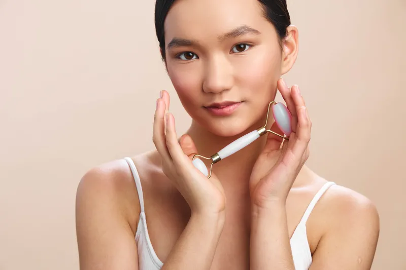 asian woman with a calm smile performs a skincare treatment using a handheld facial device in a modern studio, conveying a serene beauty routine and contemporary selfcare.
