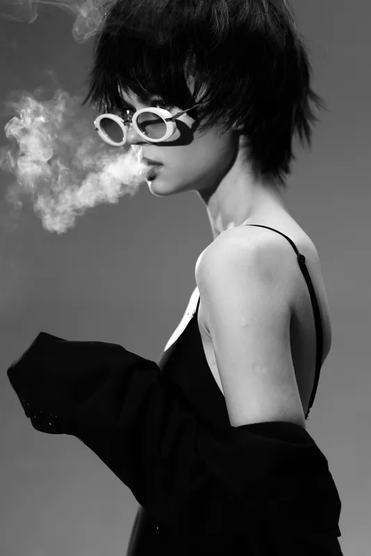 Black and white portrait of a woman smoking with retro sunglasses and short hair in a moody atmosphere