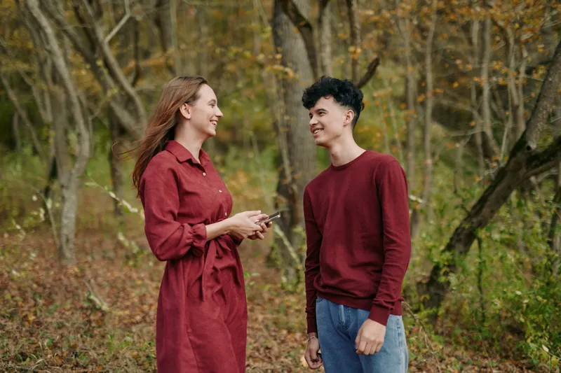Candid outdoor portrait of a young couple smiling and chatting in a wooded clearing, natural expressions and relaxed posture convey authenticity and a believable, emotionally warm connection and