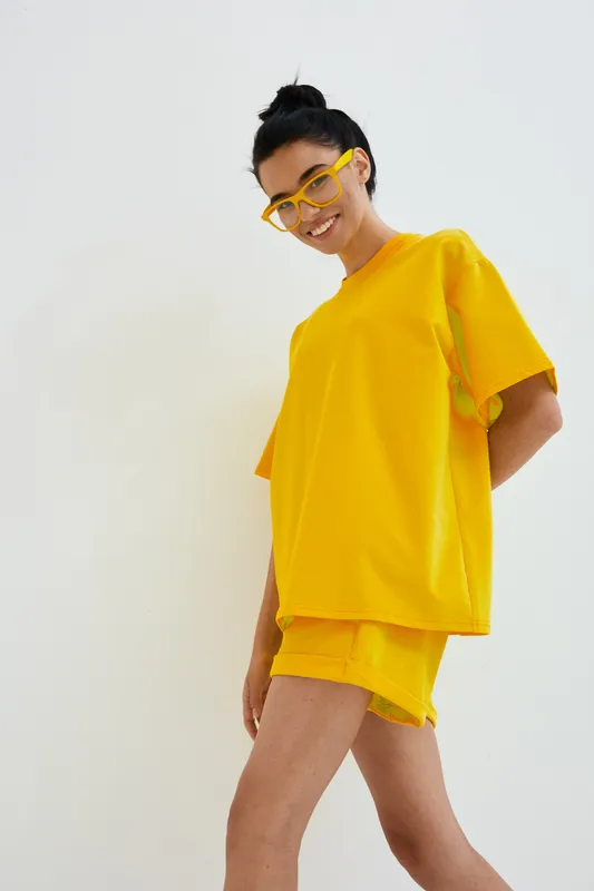 young woman in bright yellow casual outfit smiling confidently, wearing glasses, standing against clean white background, summer fashion style