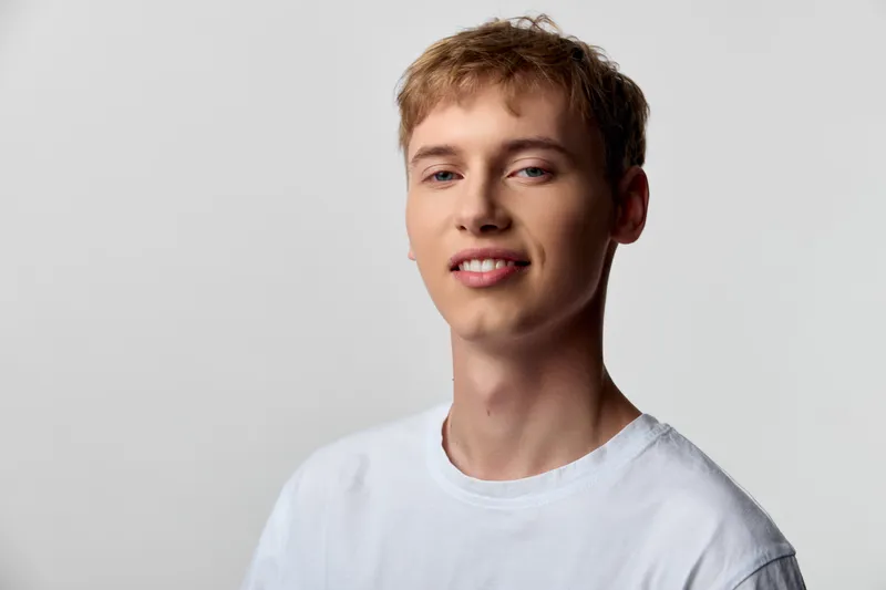 Smiling man, casual white tee, friendly expression, light background, studio lighting for a fresh, approachable mood suitable for lifestyle, fashion, or corporate uses.
