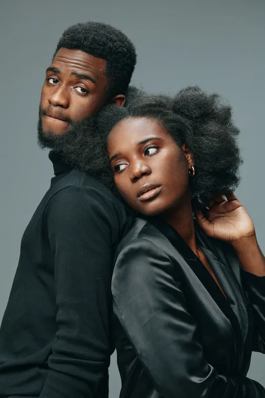 Elegant couple portrait showcasing diverse ethnicity, dressed in stylish black attire, conveying deep emotions against a soft gray backdrop