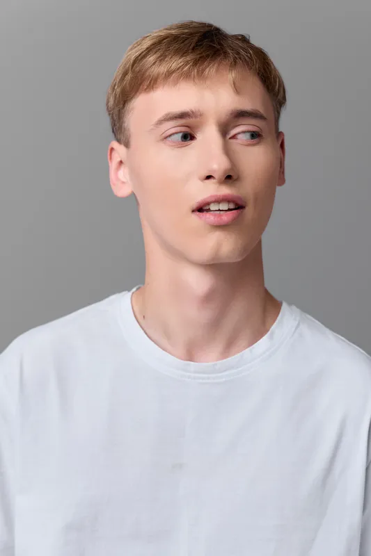Young man in a white tee in a studio, casual pose with sideways gaze and thoughtful expression, clean gray backdrop, versatile for lifestyle, fashion and commercial use.