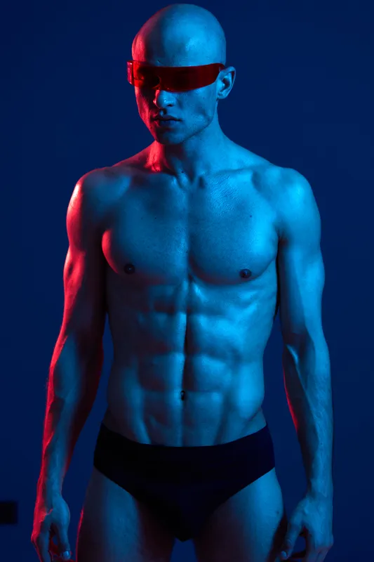 Athletic man posing in a dynamic blue and red light, showcasing a confident expression. The striking colors bring an energetic vibe to the scene.