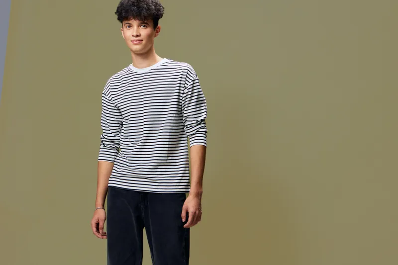 young man wearing a striped long-sleeve shirt standing against plain background with casual style and relaxed expression