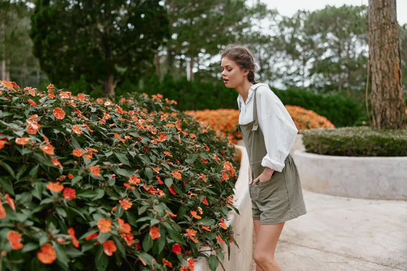 Young woman in light clothes admiring blooming flowers in a serene garden, showcasing spring beauty and connection with nature