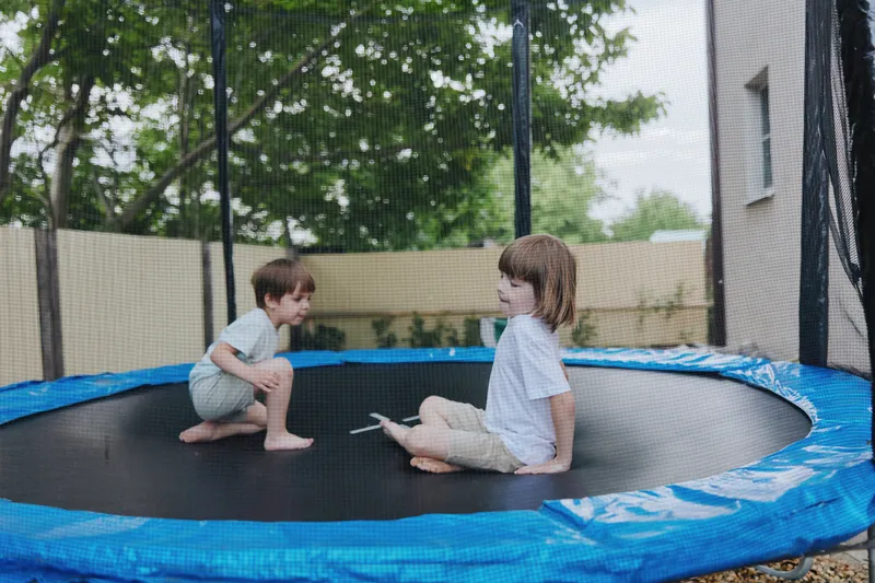 Two joyful kids playing on a trampoline in a backyard, enjoying their day outdoors with smiles and laughter, showcasing childhood happiness and movement.