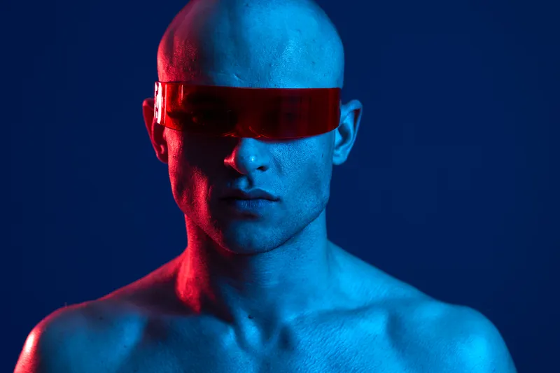 Portrait of a man with futuristic sunglasses, colored lighting creating a dramatic atmosphere, showcasing an edgy and modern vibe.