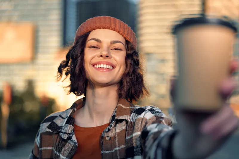 Woman smile coffee urban candid authenticity golden lifestyle portrait of a young woman holding a takeaway cup during golden hour glow, joyful mindful living and emotional storytelling in city.