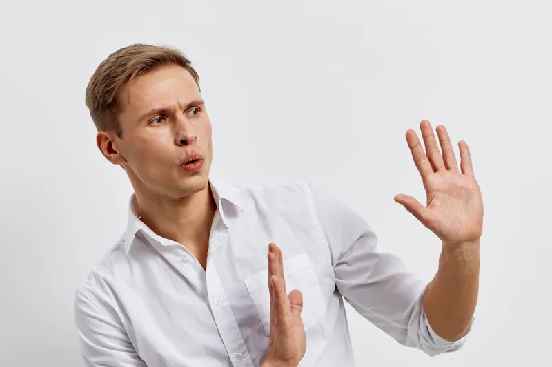 Frustrated young man with light brown hair and fair skin wearing white shirt expressing shock or disagreement with hand gestures isolated on plain white background studio portrait. People emotion conc